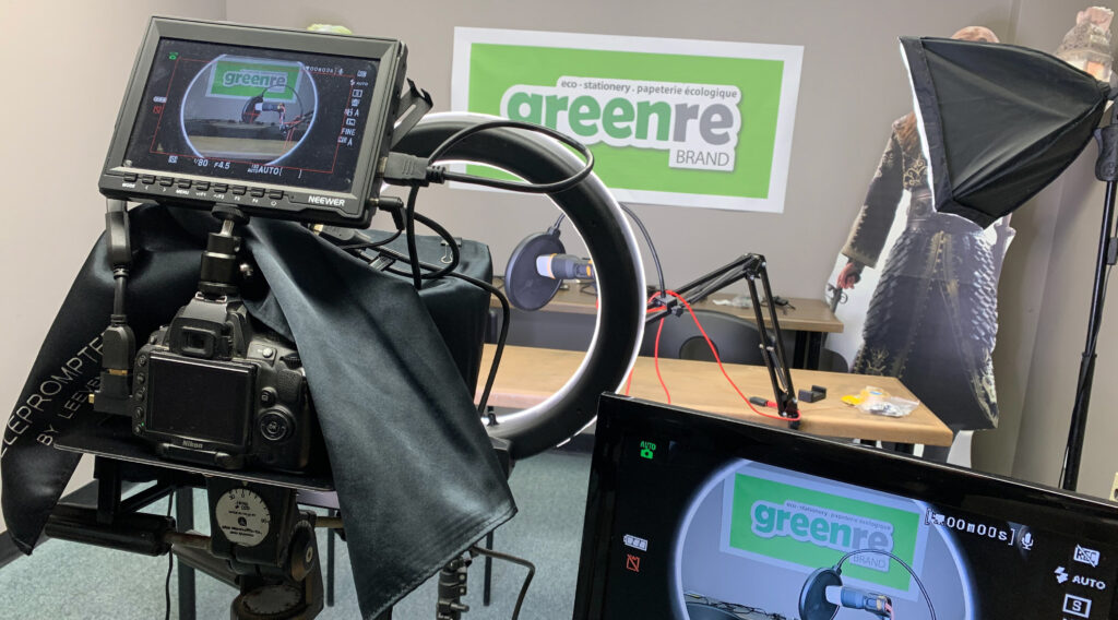 A view from behind a large video camera, pointed towards an empty table and the greenre logo on the wall.